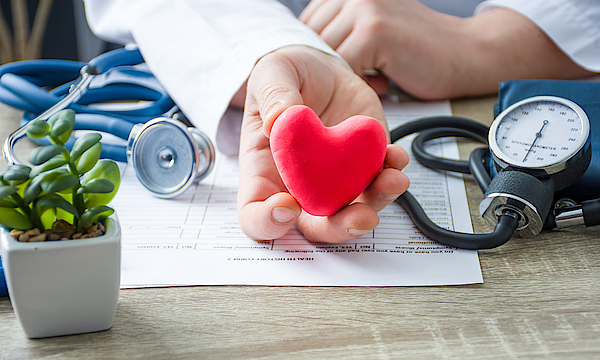 Arzt sitzt am Schreibtisch und hält ein rotes Herz in der Hand.
