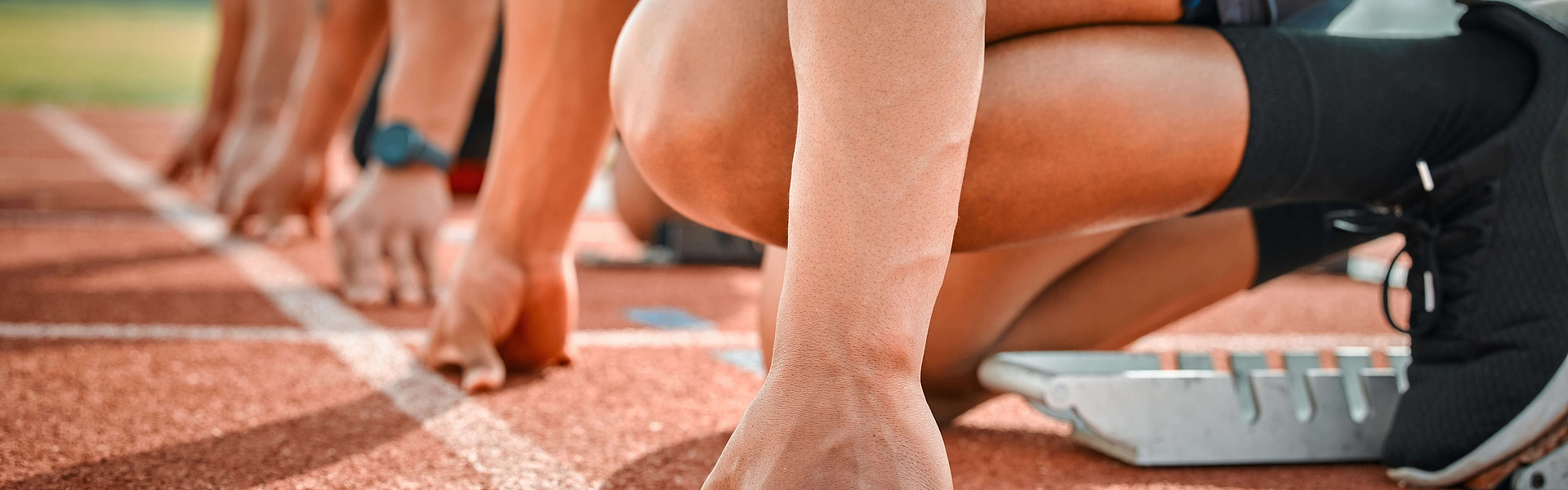 Mehrere Sportler mit einem Sportlerherz am Start einer Tartanbahn