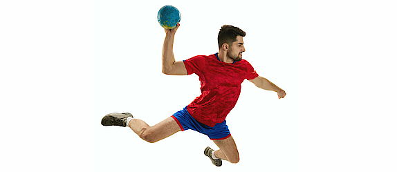 Ein Handballspieler mit einem roten Trikot ist im Sprungwurf. Der Ball ist in seiner rechten Hand. Er ist bereit zu werfen.