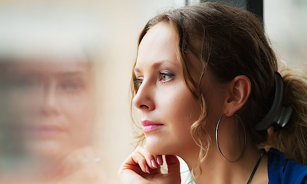 Nachdenkliche Frau, links im Bild sieht man ein verschwommenes Spiegelbild dieser Frau.