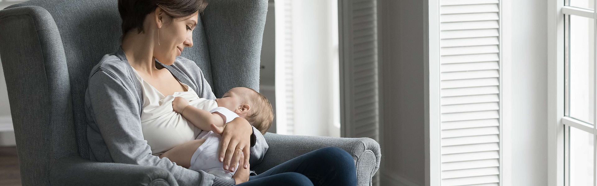 Eine Mutter sitze in einem Sessel und stillt ihr Baby