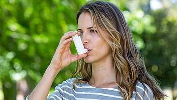 Eine Frau ist im Garten und benutzt ein Asthmaspray.