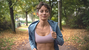 Eine Frau joggt durch den Wald. Sie nimmt über die Bonus-App an den Bonusprogrammen der mhplus teil.