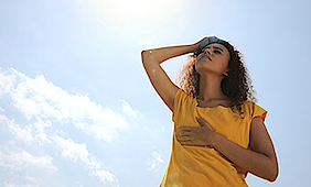 Sommerhitze, eine Frau steht in der Sonne und wischt sich mit einem Tuch über die Stirn..
