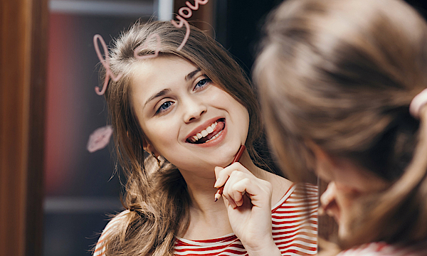 Zu sehen ist eine junge geschminkte Frau, die mit dem Lippenstift auf dem Spiegel "I love you" geschmiert hat.