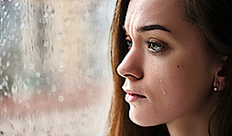 Nahaufnahme einer hübschen, weinenden Frau, die aus dem Fenster schaut. Am Fenster sind Regentropfen.