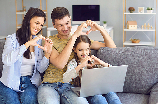 Zu sehen ist eine glückliche Familie mit einem Laptop im Wohnzimmer.