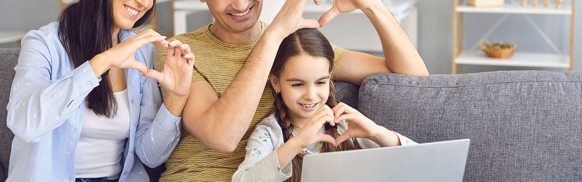 Zu sehen ist eine glückliche Familie mit einem Laptop im Wohnzimmer.
