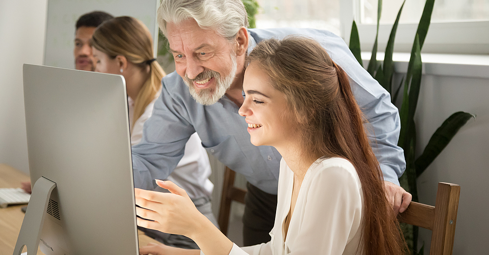 Der Chef zeigt der jungen Angestellten am Laptop wie sie die Neuigkeiten der mhplus Wissensseite für Arbeitgeber aufrufen kann.