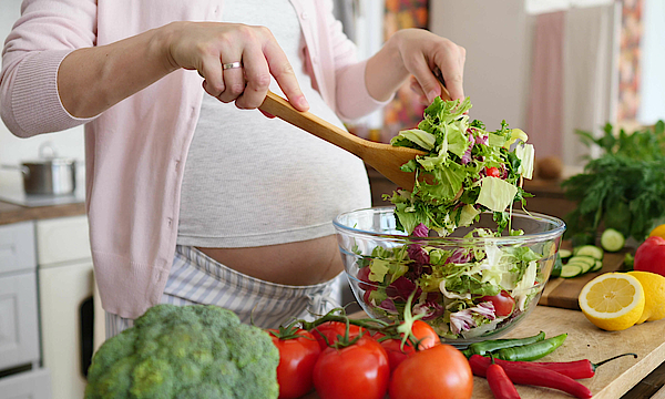 Schwangere Frau bereitet Salat vor.