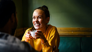 Frau sitze in einem Cafe am Tisch und unterhält sich lächelnd