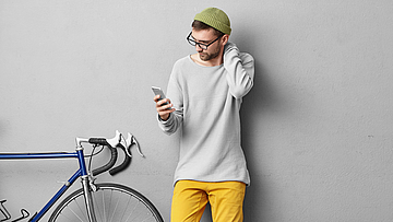 Zu sehen ist ein Mann der sich am Nacken hält und aufs Handy schaut.