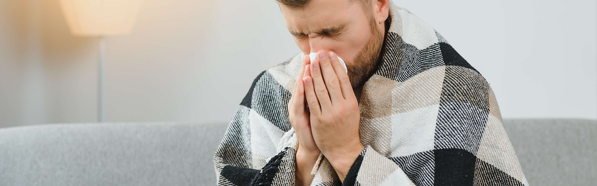 Mann sitzt auf dem Sofa und befindet sich mitten im Verlauf einer Erkältung