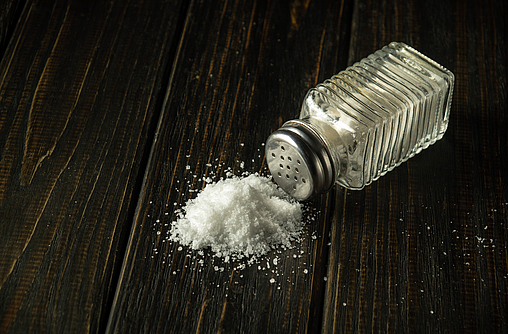 Salzstreuer liegt umgestürzt auf einem dunklen Holz, etwas von dem weißen Salz liegt auf dem Holz
