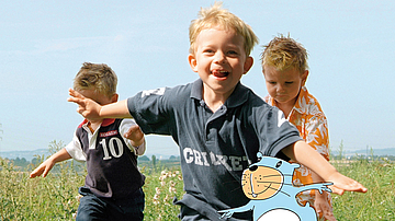 Kinder rennen auf einer Wiese und haben viel Spaß.