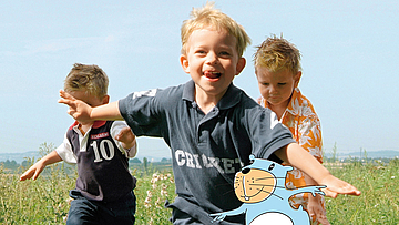 Kinder rennen auf einer Wiese und haben viel Spaß.