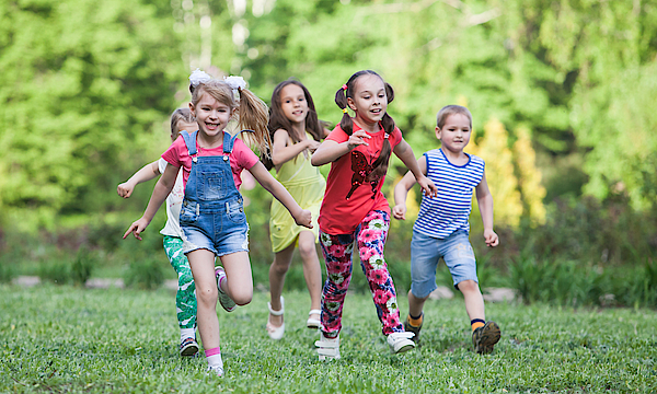 Eine Gruppe glücklicher Kinder von Jungs und Mädchen laufen im Park auf dem Gras an einem sonnigen Sommertag.