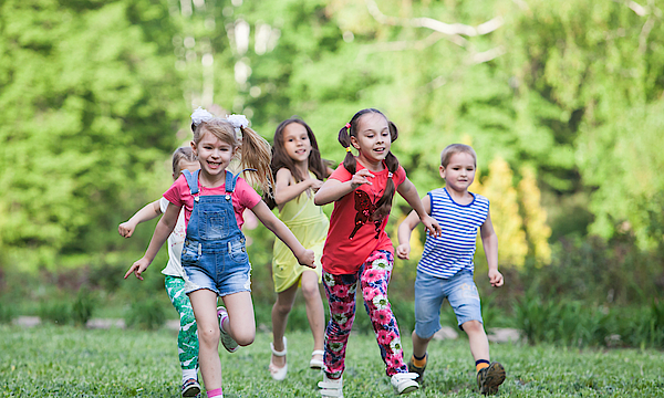 Eine Gruppe glücklicher Kinder von Jungs und Mädchen laufen im Park auf dem Gras an einem sonnigen Sommertag.