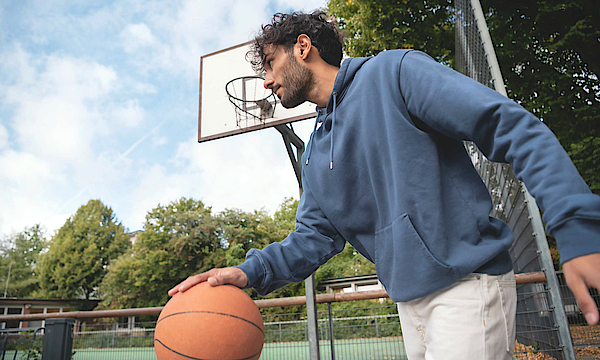 Mann prellt auf dem Sportplatz einen Basketball.