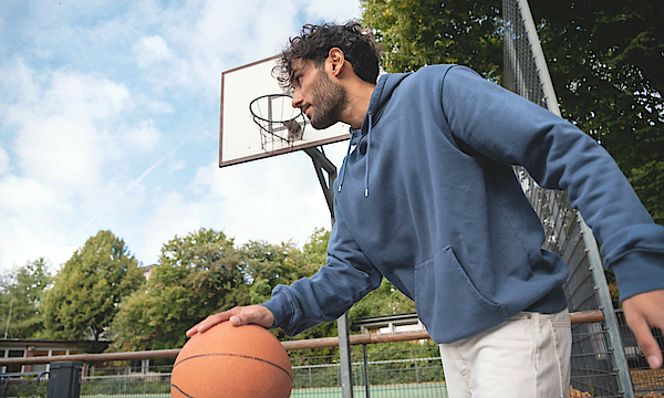 Mann prellt auf dem Sportplatz einen Basketball.