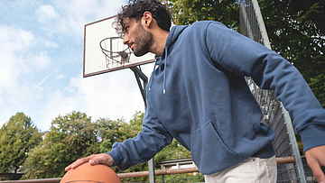 Mann prellt auf dem Sportplatz einen Basketball.