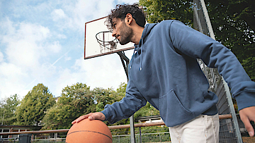 Mann prellt auf dem Sportplatz einen Basketball.