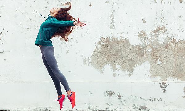 Eine junge Frau in sportlicher Kleidung springt in die Luft.