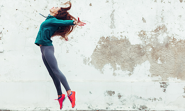 Eine junge Frau in sportlicher Kleidung springt in die Luft.