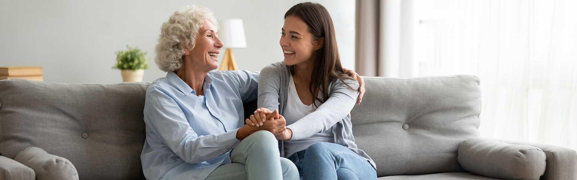 Lächelnd Seniorin umarmt Enkeltochter, die sich entspannend zu Hause fühlen.