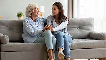 Lächelnd Seniorin umarmt Enkeltochter, die sich entspannend zu Hause fühlen.