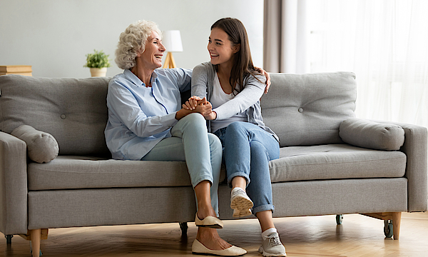 Lächelnd Seniorin umarmt Enkeltochter, die sich entspannend zu Hause fühlen.