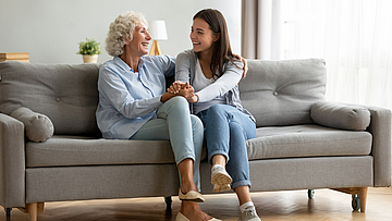 Lächelnd Seniorin umarmt Enkeltochter, die sich entspannend zu Hause fühlen.