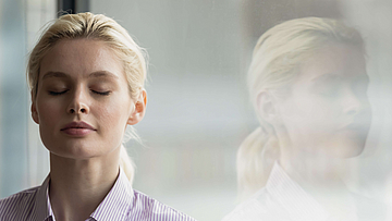 Frau steht mit geschlossenen Augen vor einem Fenster.