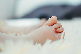 Ein Säugling liegt auf einer Decke. Zu sehen ist sein Fuß mit einem Blutschwämmchen.