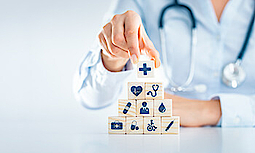 Ein Arzt stapelt Holzwürfel mit Symbolen zum Thema Gesundheit zu einer Pyramide