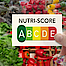 Eine Hand hält die Tabelle des Nutri Scores von A bis E in der Hand. Dahinter sieht man Gemüse.