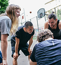 Fünf junge Männer und Frauen beugen sich auf einem Basketballfeld im Kreis einander zu