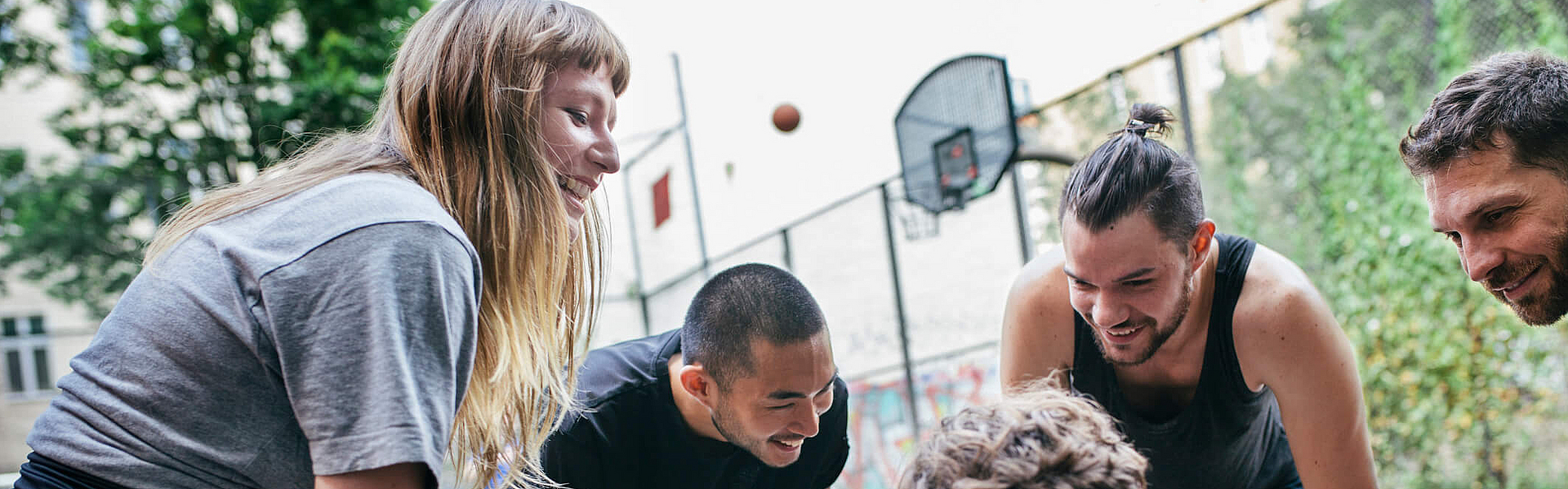 Fünf junge Männer und Frauen beugen sich auf einem Basketballfeld im Kreis einander zu