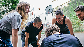 Fünf junge Männer und Frauen beugen sich auf einem Basketballfeld im Kreis einander zu