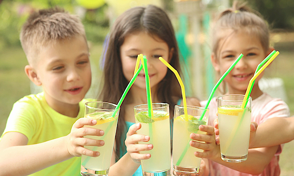Drei Kinder halten Gläser mit Zitronenlimonade in der Hand. Sie prosten sich zu. 