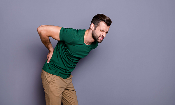 Mann vor lilafarbenem Hintergrund, er greift in den unteren Rücken. 