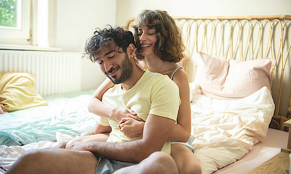 Glückliches Paar sitzt zusammen auf dem Bett.