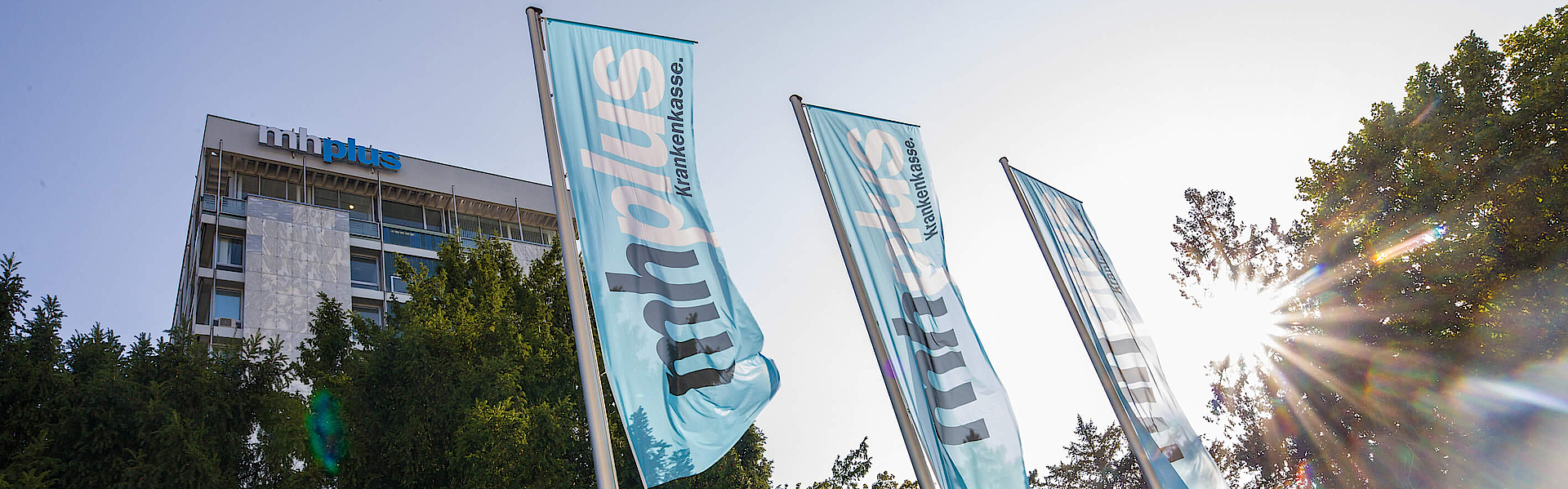 Das Bürogebäude der mhplus in Ludwigsburg mit Bäumen und drei Marken-Flaggen davor