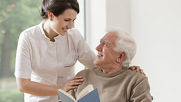 Eine junge ambulante Pflegerin pflegt einen älteren Herren zu Hause.