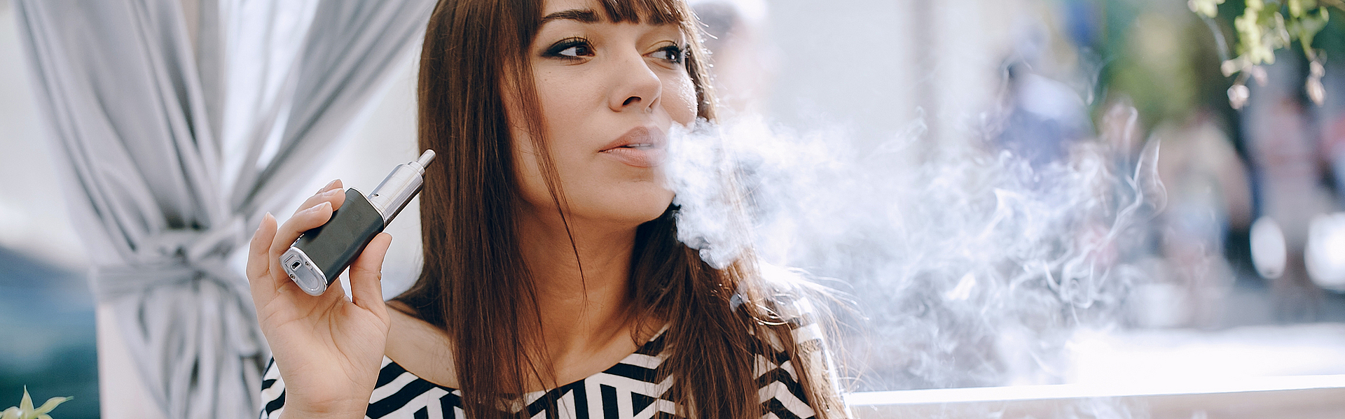 Schicke, dunkgelhaarige Frau sitzt an einem Tisch und ist beim Vapen.