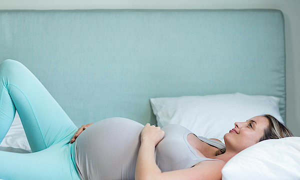 Eine schwangere Frau liegt glücklich im Bett.