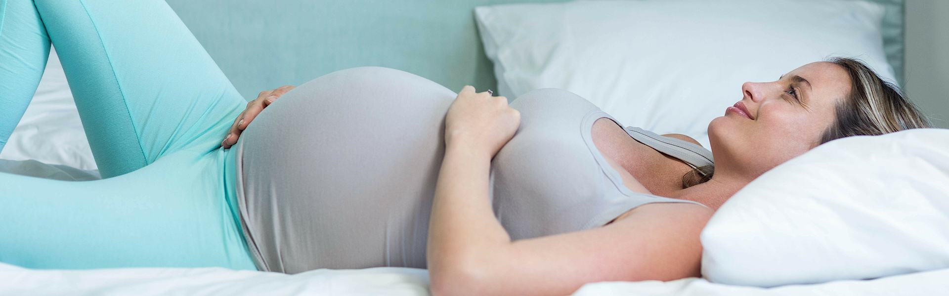 Eine schwangere Frau liegt glücklich im Bett.