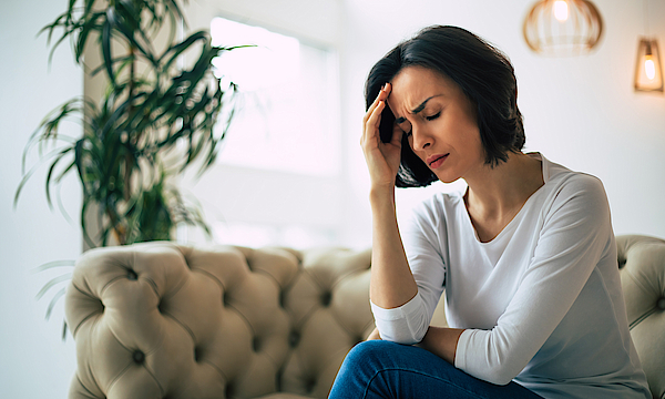 Kopfschmerzen. Nahaufnahme einer jungen Frau, die mit geschlossenen Augen auf einem Sofa sitzt und ihren Kopf berührt, während sie an einer Migräne leidet.