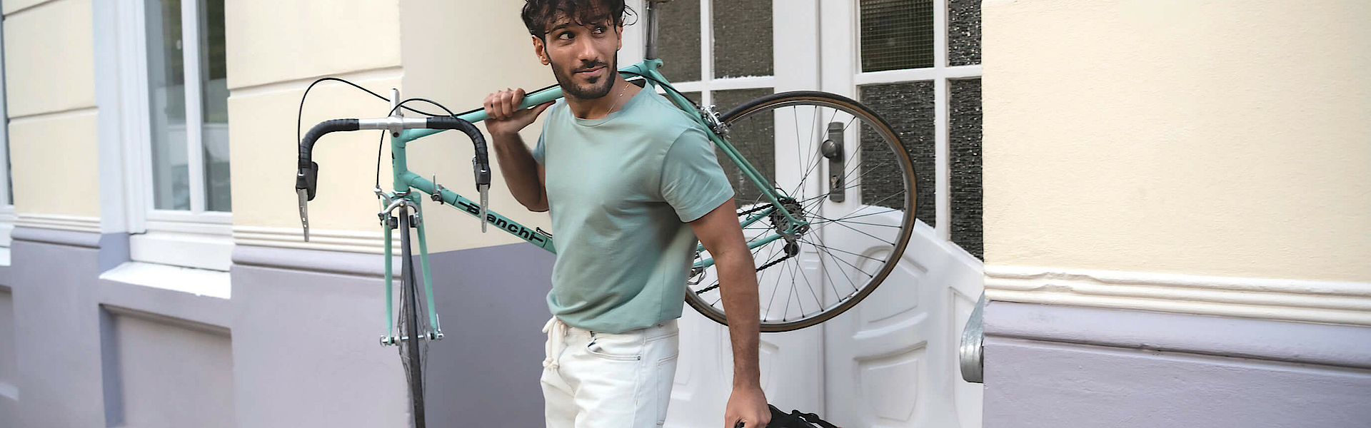 Ein Mann trägt rechts sein Fahrrad und steht auf einer Treppe. Er wendet den Blick nach links.