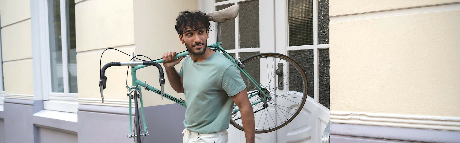 Ein Mann trägt rechts sein Fahrrad und steht auf einer Treppe. Er wendet den Blick nach links.